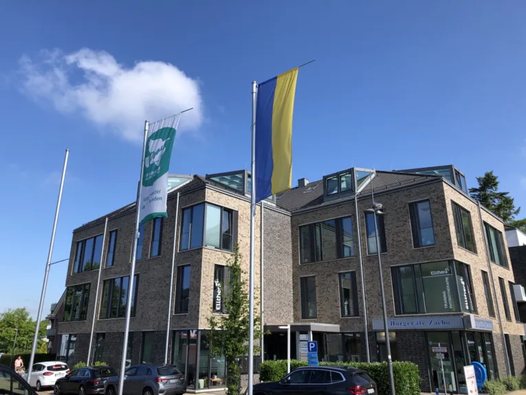 Die gr&uuml;n-wei&szlig;e-Mayors-for-Peace-Flagge weht neben einer Flagge in den ukrainischen Nationalfarben vor einem Geb&auml;ude in Halstenbek (Schleswig-Holstein) im Wind.